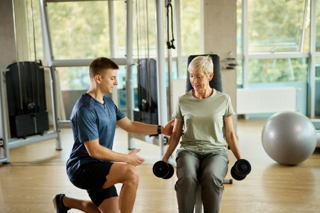 Older adult performing a strength training exercise with guidance from a personal trainer to improve strength, balance, and independence.